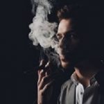 Handsome man in suit on the black background smoking a cigar
