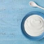 Greek yogurt in blue bowl on rustic wooden table top view.