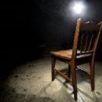 Isolated wooden chair in a dark scary prison with an interrogation spotlight