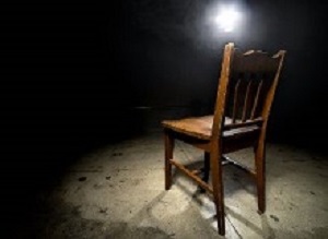 Isolated wooden chair in a dark scary prison with an interrogation spotlight