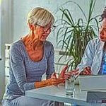 A female doctor sits at her desk and chats to an elderly female patient while looking at her  test results