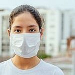 Girl, young woman in protective sterile medical mask on her face looking at camera outdoors. Air pollution, virus, Chinese pandemic coronavirus concept.