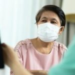 Asian Female Doctor or Nurse in green uniform talking giving advice to Elderly woman patient in pink cloth and looking to computer screen monitor