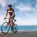 Mature Adult on a racing bike climbing the hill at mediterranean sea landscape coastal road