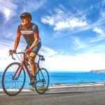 Mature Adult on a racing bike climbing the hill at mediterranean sea landscape coastal road