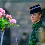 Armed forces female officer in camouflage uniform at Royal Palace guard post, flowers in foreground, Stockholm, Sweden