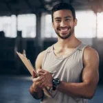Portrait of a muscular young man writing notes on a clipboard while working in a gym