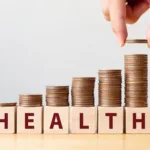 Hand putting coins on stack stair as step growing growth and wooden cube block with word HEALTH. Investment health and insurance fund concept