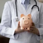 Crop close up female doctor physician holding pink piggy bank