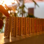 Hand poked on a row of wooden dominoes, with the words "COVID19" and "LONG COVID"