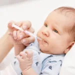 Mother feeding newborn baby with liquid Vitamin K