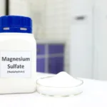 Selective focus of magnesium sulfate or epsom salt chemical compound bottle beside a petri dish with white crystalline powder in a chemistry laboratory background.